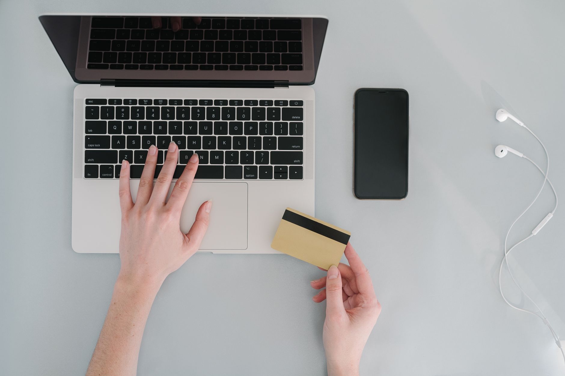 Mains utilisant le clavier d’un ordinateur portable et tenant une carte bancaire près d’un smartphone.