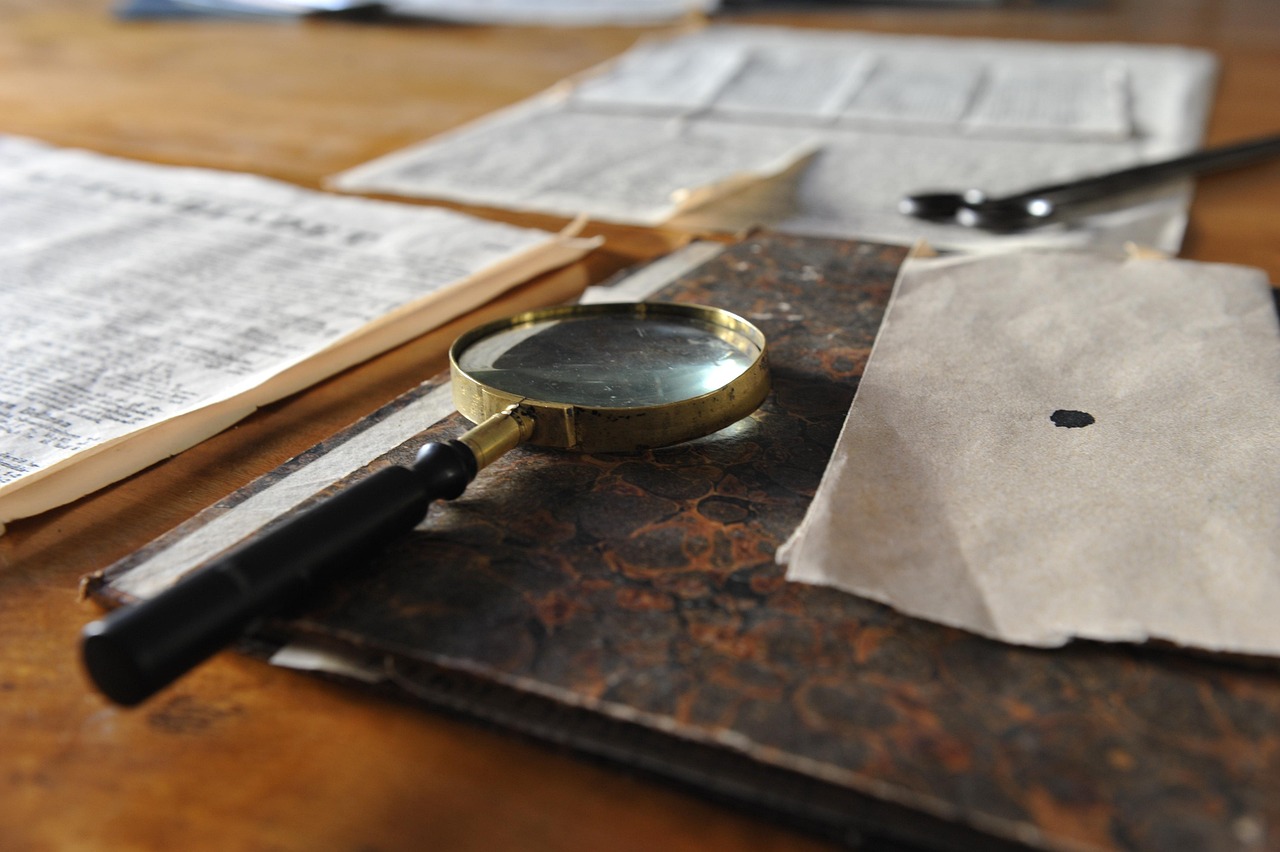 Une loupe en laiton posée sur un registre ancien relié, entourée de feuillets jaunis sur une table en bois.