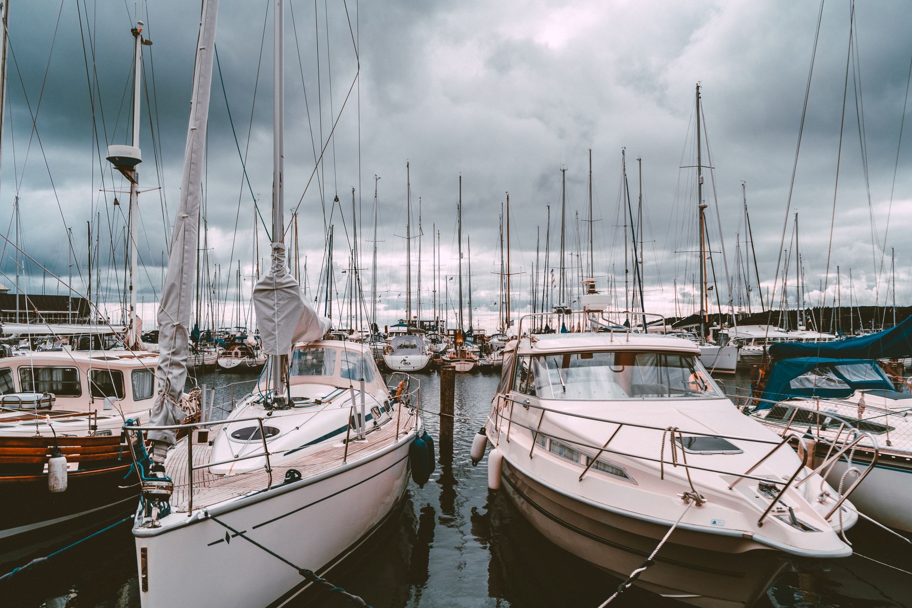 Voiliers et bateaux à moteur amarrés dans un port de plaisance, sous un ciel nuageux et sombre.
